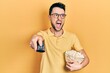 © Krakenimages.com - Young hispanic man eating popcorn using tv control angry and mad screaming frustrated and furious, shouting with anger. rage and aggressive concept.