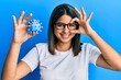 © Krakenimages.com - Young latin woman holding virus toy smiling happy doing ok sign with hand on eye looking through fingers