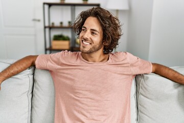 Sticker - Young hispanic man smiling happy sitting on the sofa at home.