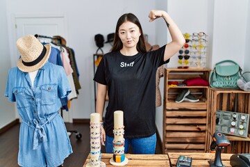 Poster - Young asian woman working as manager at retail boutique strong person showing arm muscle, confident and proud of power