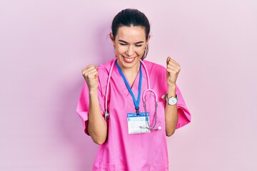 Young brunette woman wearing doctor uniform and stethoscope excited for success with arms raised and eyes closed celebrating victory smiling. winner concept.