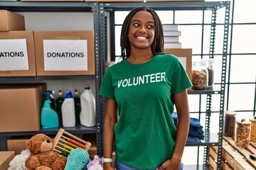 Poster - Young african american woman working wearing volunteer t shirt at donations stand looking away to side with smile on face, natural expression. laughing confident.