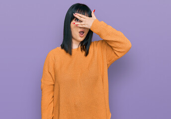 Canvas Print - Young hispanic woman wearing casual clothes peeking in shock covering face and eyes with hand, looking through fingers with embarrassed expression.