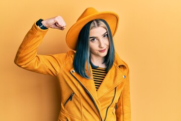 Wall Mural - Young modern girl wearing yellow hat and leather jacket strong person showing arm muscle, confident and proud of power