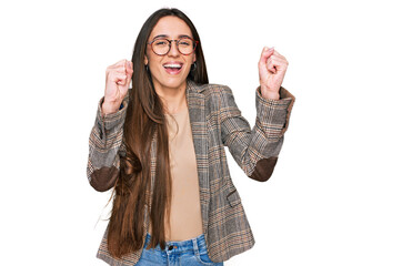 Canvas Print - Young hispanic girl wearing business clothes and glasses celebrating surprised and amazed for success with arms raised and open eyes. winner concept.