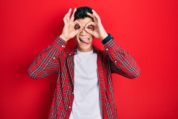 Sticker - Young hispanic man wearing casual clothes doing ok gesture like binoculars sticking tongue out, eyes looking through fingers. crazy expression.