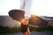 © BublikHaus - Young hipster man holds cool longboard in hand. Sun sunset light leak in lens. Beautiful travel wanderlust concept. Millennial adventure trip. Skater walk with skateboard