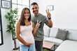 Young interracial couple expecting a baby, touching pregnant belly smiling looking to the camera showing fingers doing victory sign. number two.