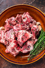 Raw mutton meat diced for goulash or stew with bone on a rustic plate. Dark background. Top view