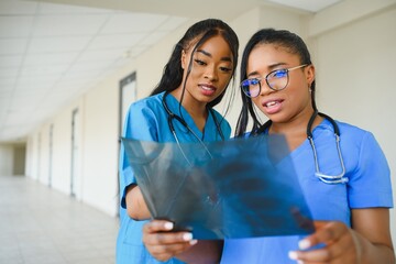 Beautiful female and handsome Afro American doctors are examining X-ray photograph, two other doctor are talking in the background