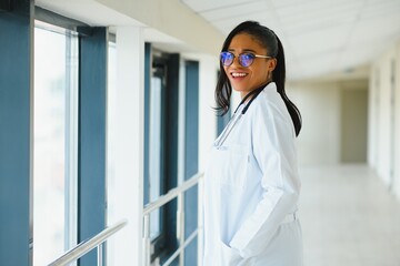 Wall Mural - portrait of friendly, smiling confident female healthcare professional with lab coat, arms crossed holding glasses. Isolated hospital clinic background.