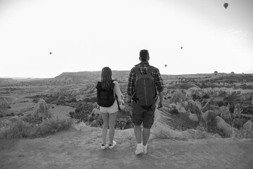 Black and white. Tourist couple, man and woman enjoy the view. Balloon flight at background. Entertainment, tourism an vacation. Travel tour. Goreme, Cappadocia, Turkey.