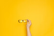 © Shi  - Hands hold stylish creative glasses for vision on yellow background. Eyesight optician concept
