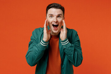 Wall Mural - Promoter fun young brunet man 20s wears red t-shirt green jacket scream hot news about sale discount with hands near mouth isolated on plain orange background studio portrait. People emotions concept