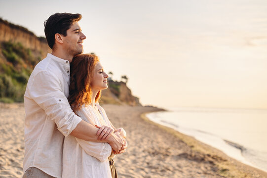 Profile happy romantic satisfied smiling young couple two friends family man woman 20s in white clothes hug rest together at sunrise over sea beach ocean outdoor seaside in summer day sunset evening