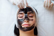 © руслан малыш - cosmetologist applying black mask on pretty woman face wearing black gloves, gorgeous woman in spa having facial procedures