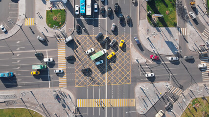 Wall Mural - Beautiful view from above to a busy crossroad in a big city. Camera moving upwards showing cars and trucks turning at the intersection while others waiting at the traffic lights.