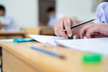 Wall Mural - Asian Student using rubber eraser in writing learning Exams in classroom. at high school of education. School student's read note taking assessment writing on answer papers for asmission in classmates