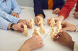 © Studio Romantic - Close up of business team members joining wooden human figures around toy space rocket on office table. Metaphor for teamwork. Symbol of developing group projects and launching new products together
