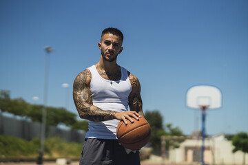 Wall Mural - Handsome caucasian basketball player with cool tattoos standing on the court holding the ball