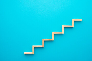 Flat lay of wooden blocks in shape of staircase step on blue background with copy space. Growth or development step by step for successful in business financial or education concept.