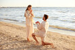 © Syda Productions - love and people concept - smiling young man with engagement ring making proposal to happy woman on beach
