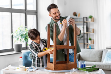 family, diy and home improvement concept - happy smiling father and son with ruler measuring old round wooden table for renovation at home