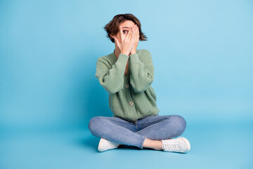 Poster - Photo of cute scared young lady dressed green cardigan sitting legs folded arms cover face isolated blue color background