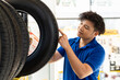 Asian male worker checking new tire wheel on shelves shelf at wheel store. Salesman examining new tire at workshop. Car service and Maintenance concept
