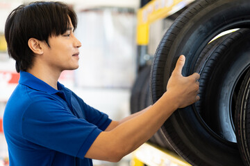Wall Mural - Asian male worker checking new tire wheel on shelves shelf at wheel store. Salesman examining new tire at workshop. Car service and Maintenance concept