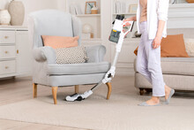 Woman Cleaning Home Carpet In Interior Under Armchair With Wireless Vacuum Cleaner. House Cleaning.