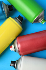 Poster - Cans of different graffiti spray paints on light blue background, flat lay