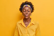 Beautiful dark skinned Afro American woman with puckered lips waits for kiss has romantic mood shows affection wears shirt and headband poses against vivid yellow background sends mwah to you