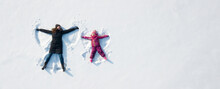 Child Girl And Mother Playing And Making A Snow Angel In The Snow. Top Flat Overhead View
