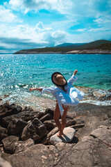 Beautiful woman seen from behind standing on a stone beach on the shore of Vis island in Croatia. Waving her arms hapily while posing, standing on one leg and meditating in amazing summer weather