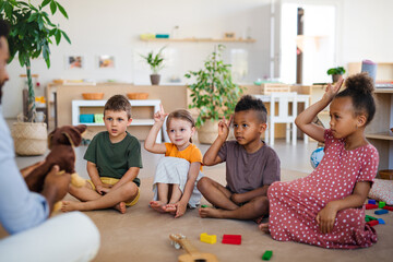 group of small nursery school children with man teacher sitting on floor indoors in classroom, raisi