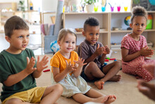 Group Of Small Nursery School Children Sitting On Floor Indoors In Classroom, Clapping.