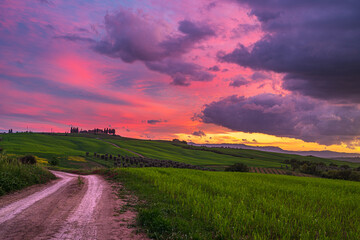 Naklejka na meble Unique green landscape in Tuscany, Italy. Dramatic sunset sky, dirt road crossing cultivated hill range and cereal crop fields.