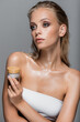 © LIGHTFIELD STUDIOS - wet woman with blonde hair holding cosmetic cream isolated on grey
