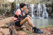 Traveling man drinking from hydration pack near waterfall in woods