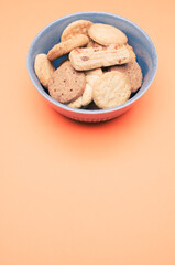 Poster - Vertical shot of organic biscuits in a blue bowl on orange background