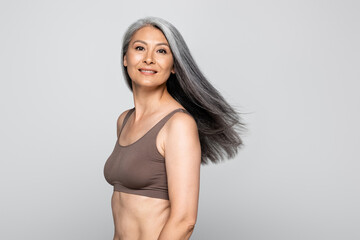 Asian woman in bra smiling at camera isolated on grey, body positive concept