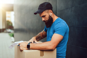 Wall Mural - A young bearded delivery man carries a package to a customer's home address.