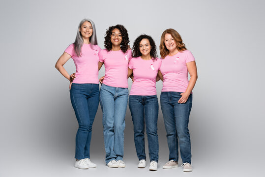 Smiling interracial women with ribbons of breast cancer awareness on grey background