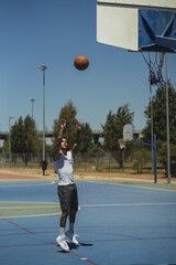 Wall Mural - Vertical shot of a caucasian guy with cool tattoos throwing the basketball ball to the hoop