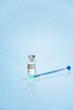 © Facundo - Vial, frasco y jeringa con medicamento vacuna Covid-19 fondo azul claro