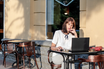 A young woman is sitting at a laptop in a summer street cafe. people using social media