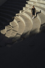 Sticker - Vertical shot of a sporty guy in black summer clothes walking on the stair with shadows