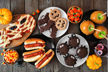 Poster - Halloween party food table scene over a rustic wood background. Overhead view. Spooky mummy pizzas, finger hot dogs, caramel apples, cupcakes, candy, cookies and donuts.
