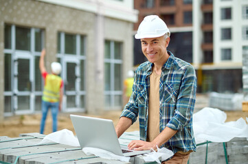 Wall Mural - Joyous male working on his laptop on the building site